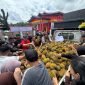 Ratusan warga tampak berkerumun di sekitar mobil bak terbuka yang dipenuhi gunungan durian, saling berebut dengan tertib dan penuh kegembiraan untuk dimakan bersama.
